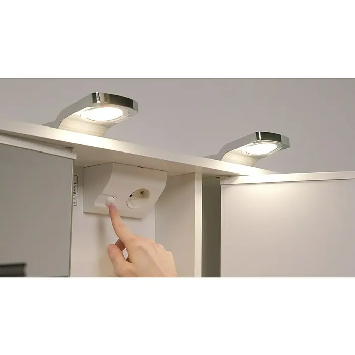 Jokey LED-Spiegelschrank Lena - B x H: 80 x 64 cm, Holz, Weiß - Nahaufnahme eines Badezimmerspiegelschranks mit integrierter Beleuchtung und Steckdose, eine Hand betätigt den Lichtschalter.