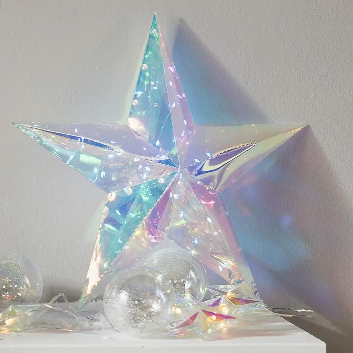 Tween Light Lámpara LED decorativa con caja de regalo - Multicolor, L x An x Al: 19 x 19 x 38 cm, Árbol - Estrella de Navidad holográfica iridiscente, iluminada con luces delicadas, junto a bolas transparentes sobre una superficie blanca.