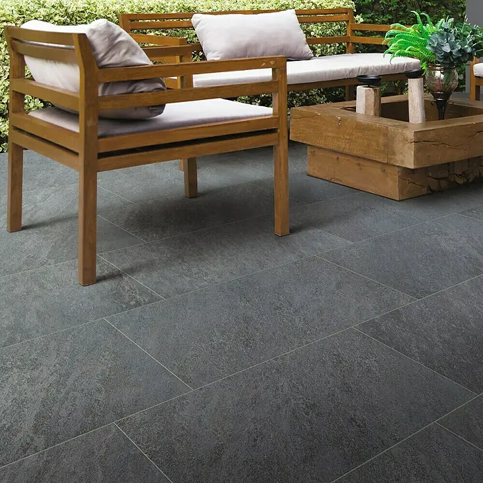 Feinsteinzeugfliese Skiffer - 30 x 60 cm, Anthrazit, Matt - Terrassenansicht mit grauen Bodenfliesen im Außenbereich, die eine moderne und stilvolle Atmosphäre schaffen. Gartenmöbel aus Holz ergänzen das Design.