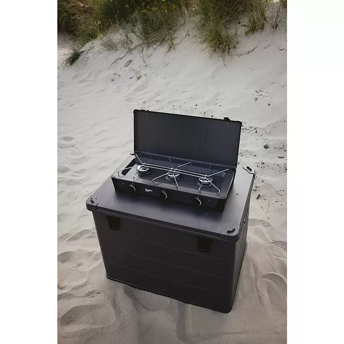 Enders Gaskocher Bondy 3Z - 61 x 32 x 33 cm, 2,3 kW, Stahl, Anzahl Brenner: 3 Stk., mit Zündsicherung - Dunkelgrauer Enders tragbarer 3-Flammen-Gaskocher auf passender Aufbewahrungsbox, im Freien im Sand.