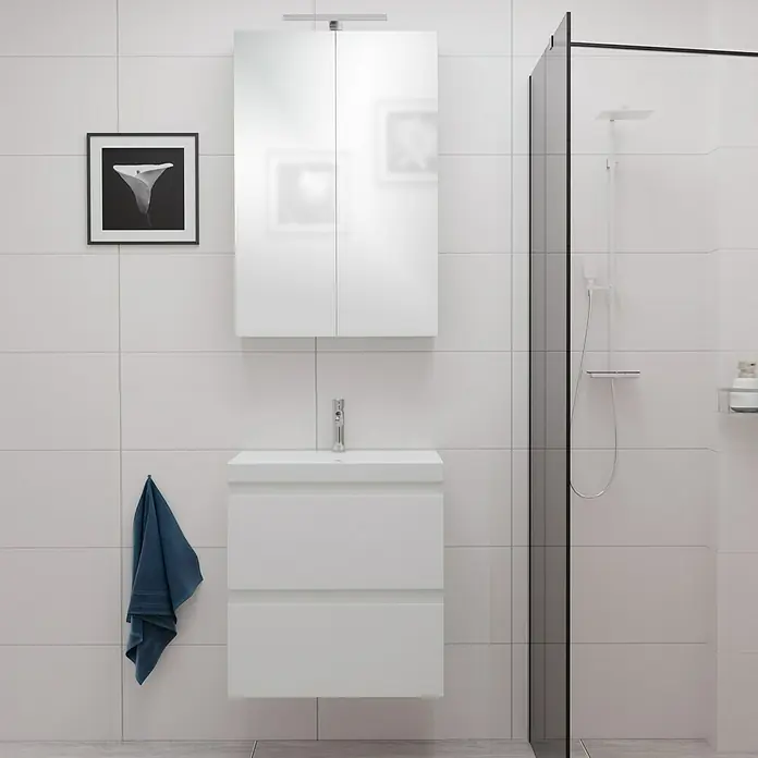 Camargue Espacio Badmöbel-Set E32 - 60 cm, Gama weiß glänzend - Ein modernes Badezimmer mit einem weißen Waschtisch mit Unterschrank und einem Spiegelschrank. An der Wand hängt ein dunkles Bild und ein blaues Handtuch.