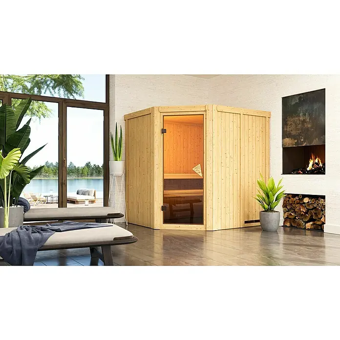 Karibu Elementsauna Siirin - Mit 9 kW Ofen mit integrierter Steuerung, Ohne Dachkranz, Materialspezifizierung Tür: Ganzglas Bronze, L x B x H: 196 x 170 x 192 cm - Innenaufnahme eines modernen Saunaraums mit Holzsauna, Kamin und Blick auf einen See. Entspannende Atmosphäre mit Pflanzen und Liegen.