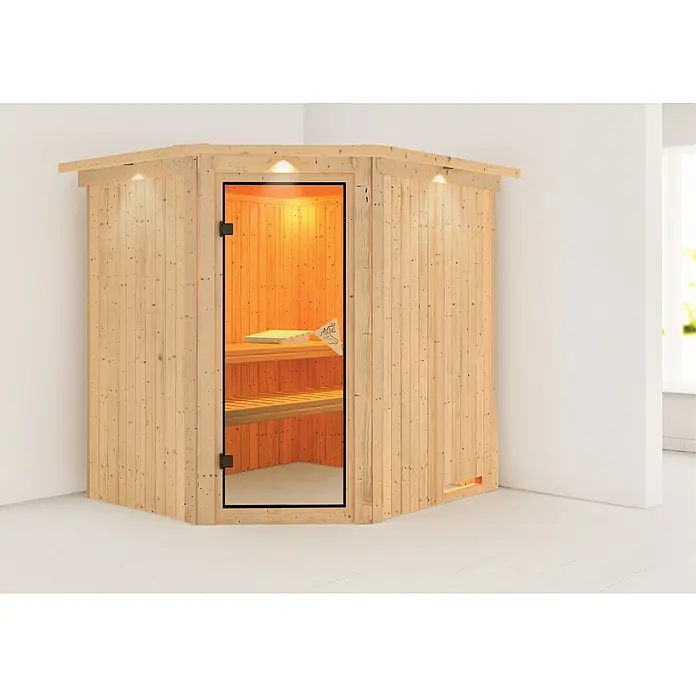 Karibu Elementsauna Siirin - Ohne Ofen, Mit Dachkranz und Beleuchtung, Materialspezifizierung Tür: Ganzglas Bronze, L x B x H: 210 x 184 x 192 cm - Eine Ecksauna aus hellem Holz mit Glastür und eingebauten Bänken, beleuchtet mit warmem Licht, steht in einem Raum mit weißen Wänden.