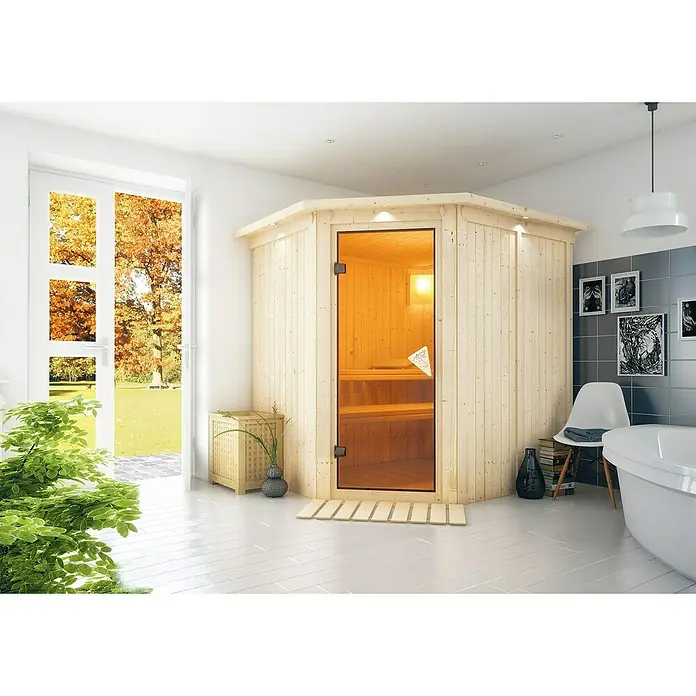 Karibu Elementsauna Siirin - Ohne Ofen, Mit Dachkranz und Beleuchtung, Materialspezifizierung Tür: Ganzglas Bronze, L x B x H: 210 x 184 x 192 cm - Helle Sauna aus Holz mit Glastür in einem Badezimmer mit weißen Fliesen und Blick ins Grüne. Entspannung pur für Zuhause.