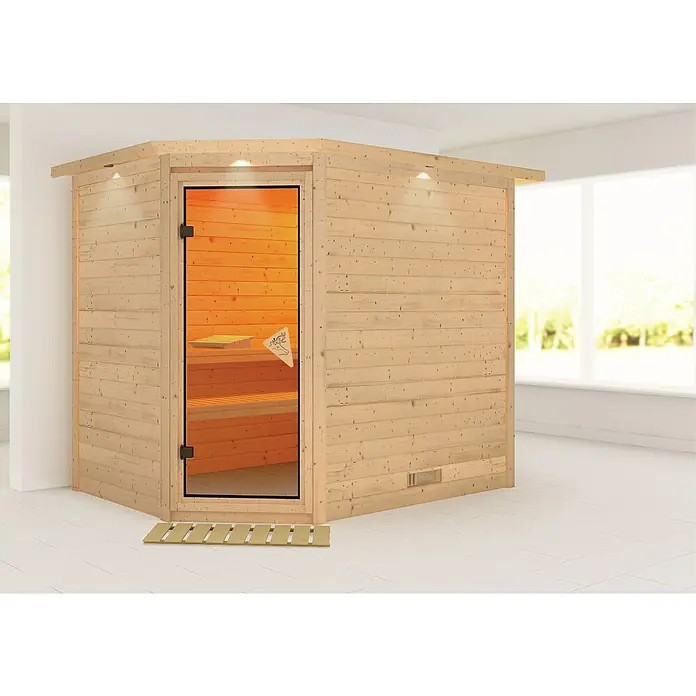 Karibu Massivholzsauna Tanami - Ohne Ofen, Mit Dachkranz und Beleuchtung, L x B x H: 259 x 210 x 192 cm - Ecksauna aus hellem Holz mit Glastür und Holzfußmatte im Badezimmer.