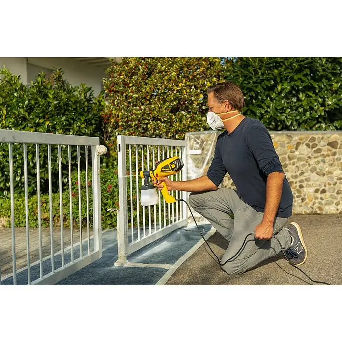 Wagner Farbsprühsystem W 590 Flexio - 630 W, Förderleistung: 0,5 l/min - Ein Mann benutzt eine Wagner Farbspritzpistole, um ein Metalltor zu lackieren, und trägt dabei eine Gesichtsmaske.