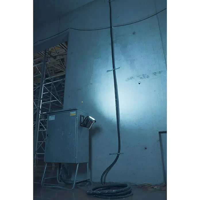 Brennenstuhl Taschenlampe Multi Akku - 21,4 x 22,5 x 19,5 cm - Ein robustes Schaltgerät mit einem hellen Arbeitsscheinwerfer, flankiert von einer Kabelrolle und einer vertikalen Kabelführung an der Wand.