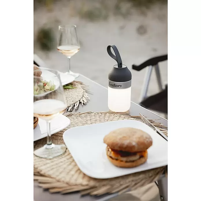 Enders Campinglampe Luvo - 100 lm - Schwarze und silberne Enders Laterne auf einem Esstisch im Freien, spendet warmes Licht neben einem Gericht und Wein.