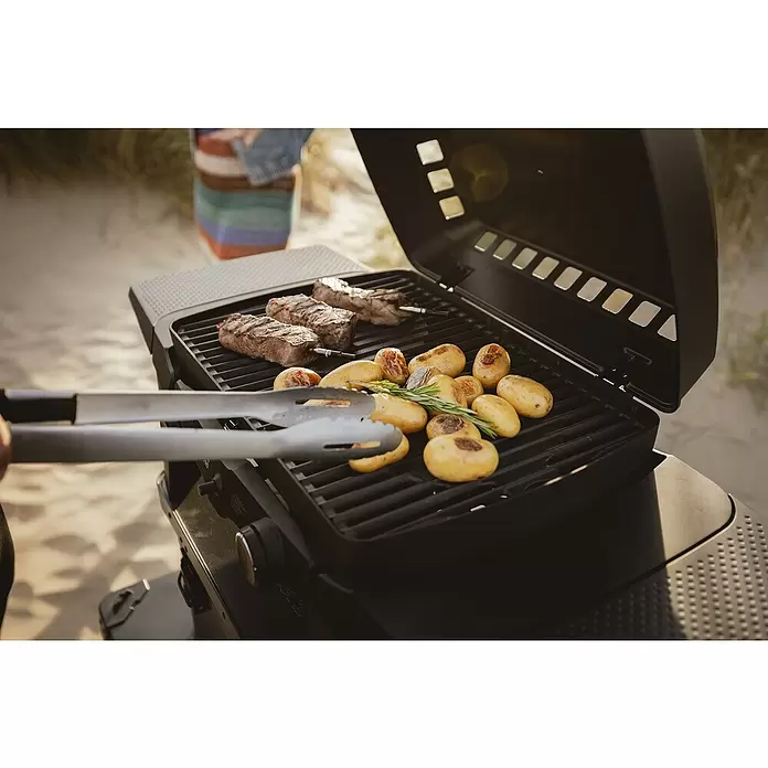 Enders Gasgrill Urban II - Grillfläche (B x T): 49 x 32 cm, 4,4 kW, Anzahl Brenner: 2 Stk. - Schwarzer Grill mit Steaks, Kartoffeln und Rosmarin. Eine Hand benutzt eine Zange.