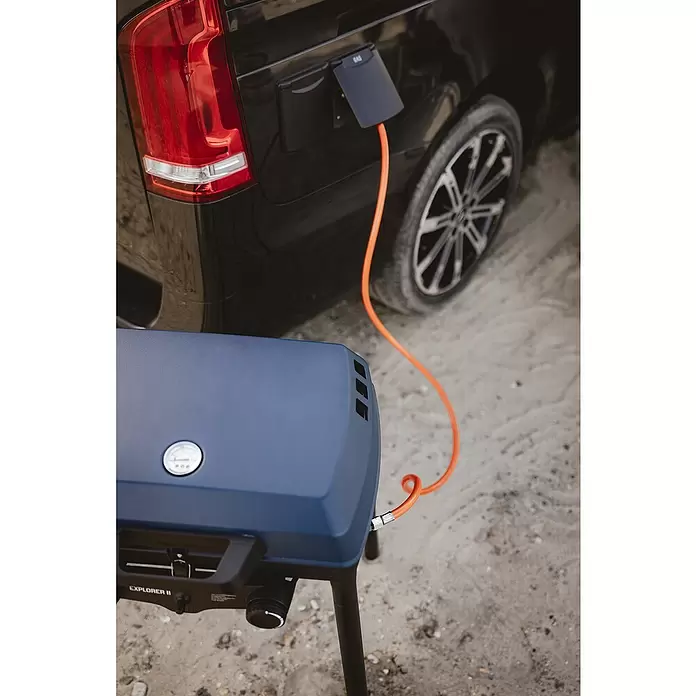 Enders Gasgrill Explorer II Caravan - Grillfläche (B x T): 49 x 32 cm, 4 kW, Anzahl Brenner: 2 Stk., 30 mbar - Ein blauer tragbarer Gasgrill, Modell EXPLORER II, über einen orangefarbenen Schlauch an den Gasanschluss eines schwarzen Fahrzeugs angeschlossen, auf sandigem Untergrund.