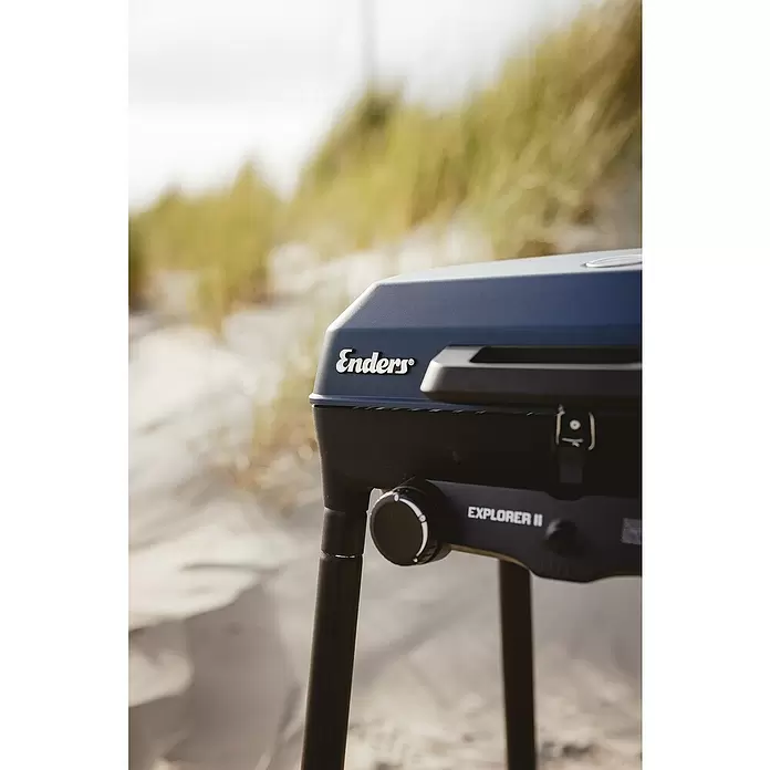Enders Gasgrill Explorer II - Grillfläche (B x T): 49 x 32 cm, 4 kW, Anzahl Brenner: 2 Stk., 50 mbar - Dunkelgrauer Enders Explorer II Gasgrill steht auf Sandboden mit Gras im Hintergrund.