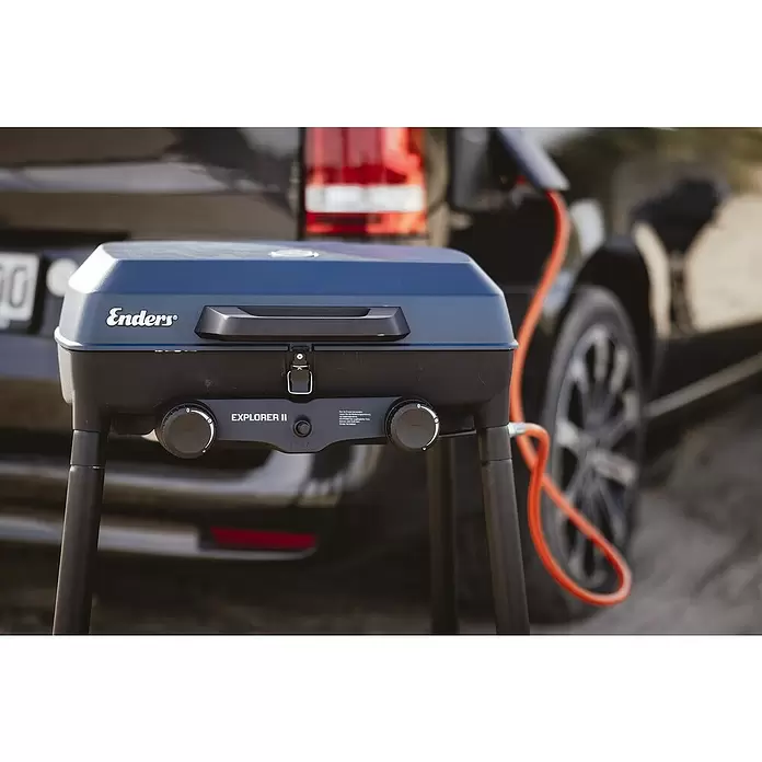 Enders Gasgrill Explorer II Caravan - Grillfläche (B x T): 49 x 32 cm, 4 kW, Anzahl Brenner: 2 Stk., 30 mbar - Dunkelblauer Enders Explorer II Gasgrill, mit orangefarbenem Schlauch an Fahrzeug angeschlossen, bereit zum Outdoor-Kochen.