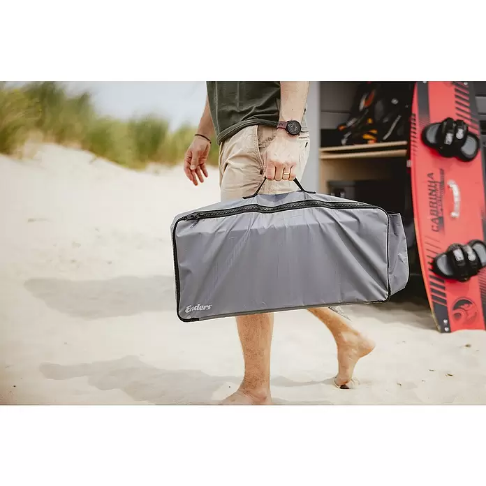 Transporttasche - Passend für: Enders Gaskocher Bondy 2, PVC - Person geht am Sandstrand, hält eine graue Enders Tragetasche mit Reißverschluss; ein rotes Kiteboard ist im Hintergrund zu sehen.