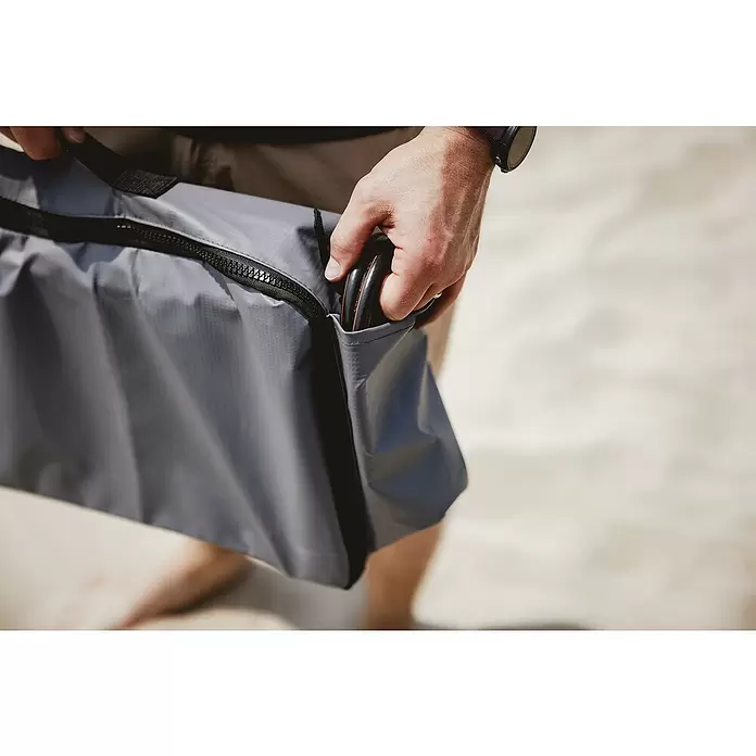 Transporttasche - Passend für: Enders Gaskocher Bondy 2, PVC - Person hält eine graue, texturierte Tasche mit schwarzem Reißverschluss und steckt einen schwarzen zylindrischen Gegenstand in die Seitentasche.