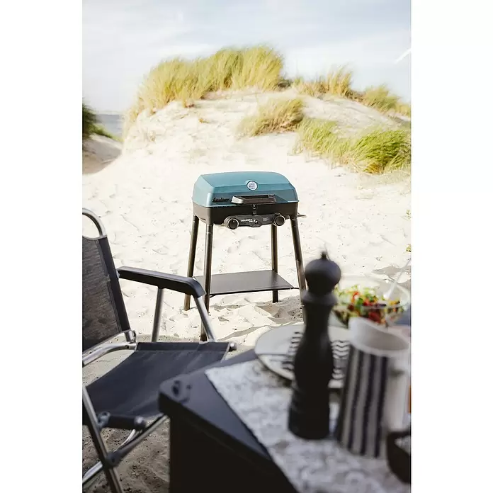 Enders Gasgrill Explorer II Pro Caravan - Grillfläche (B x T): 49 x 32 cm, 4,4 kW, Anzahl Brenner: 2 Stk., 30 mbar - Teal und schwarzer tragbarer Gasgrill auf einem Ständer am Sandstrand für eine Mahlzeit im Freien.