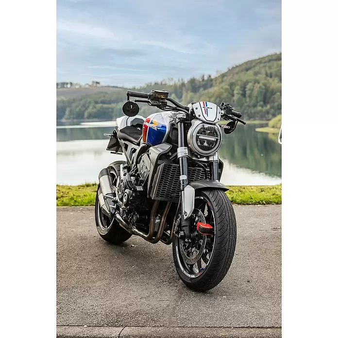Abus Bremsscheibenschloss GRANIT™ Detecto One 8078 2.0 - Geeignet für: Motorrad, Rot - Honda Motorrad mit rot-weiß-blauem Tank, rundem LED-Scheinwerfer, an einem See geparkt.