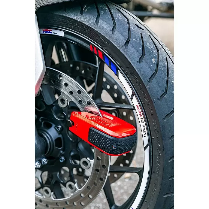 Abus Bremsscheibenschloss GRANIT™ Detecto One 8078 2.0 - Geeignet für: Motorrad, Rot - Rotes Motorrad-Bremsscheibenschloss mit schwarzem Griff, an der vorderen Bremsscheibe eines Motorrads befestigt.