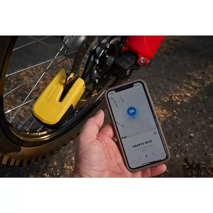 Abus Bremsscheibenschloss GRANIT™ Detecto One 8078 2.0 - Geeignet für: Motorrad, Gelb - Gelbes ABUS Bremsscheibenschloss an einem Motorradrad, dessen intelligente Funktionen auf einem Smartphone mit Standort und „verriegeltem“ Status angezeigt werden.