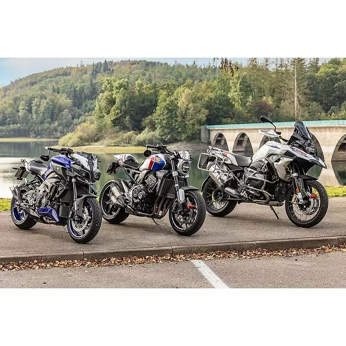 Abus Bremsscheibenschloss GRANIT™ Detecto One 8078 2.0 - Geeignet für: Motorrad, Rot - Drei unterschiedliche Motorräder: eine blaue Yamaha MT-10, eine weiß/rot/blaue Honda CB1000R und eine weiße BMW R 1250 GS, im Freien geparkt.