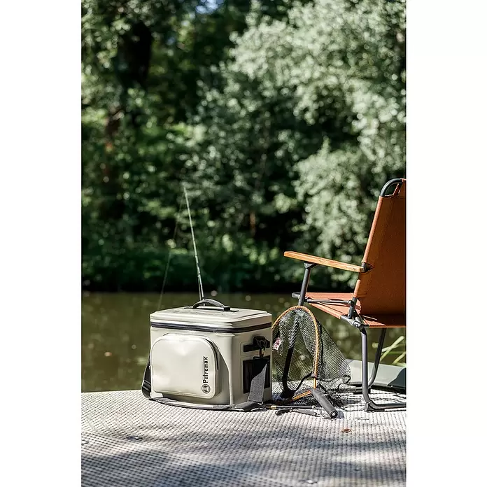 Petromax Nevera portátil - Arena, 8 l, L x An x Al: 32,5 x 25 x 28 cm - Nevera Petromax beige claro junto a una caña de pescar, red y silla junto al agua, lista para una salida de pesca.