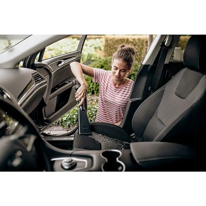 Kärcher Aspirador en seco y húmedo eléctrico KWD 3 S V-17/4/20 Aniversario - 1.000 W, Volumen de recipiente: 17 l, Con bolsa - Una mujer está aspirando el interior de un coche con una aspiradora negra. La aspiradora tiene una boquilla.