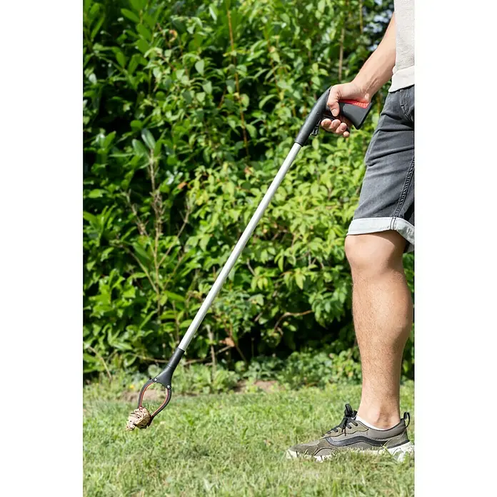 Greifer mit Magnet - Länge: 90 cm - Eine Person benutzt eine Greifzange, um ein Stück Müll vom Rasen aufzuheben, wobei der Fokus auf der Funktionalität des Werkzeugs liegt.