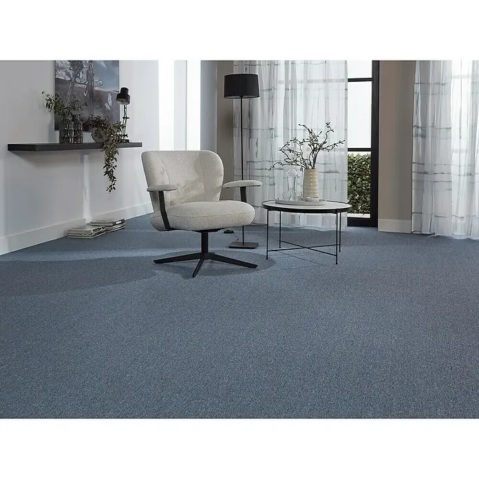 Teppichfliese Solid - Schlinge, 100 % Polyamid SDN, Blau - Das Bild zeigt einen modernen Teppich in einem Wohnzimmer mit einem Sessel, einem Tisch und einer Stehlampe. Der blaue Teppich ist das zentrale Element.