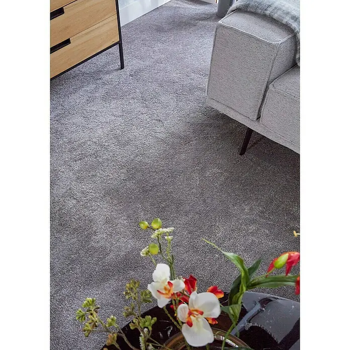 Teppichfliese Amazing - Hochflor, 100 % Polyester, Hellgrau - Nahaufnahme eines grauen Teppichs neben einem Holzschrank und einem grauen Sofa, der Komfort und Stil für das Zuhause bietet.