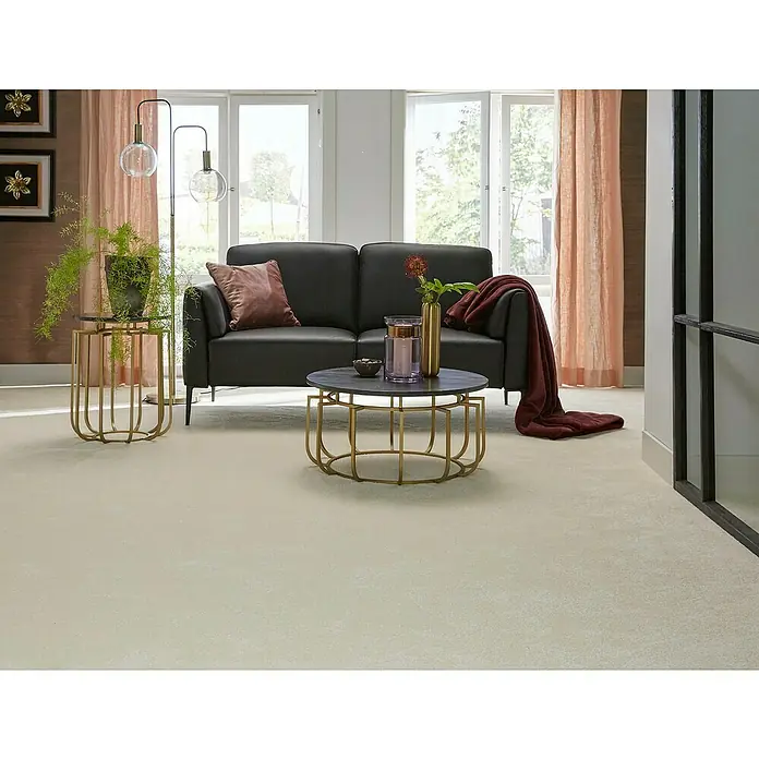 Teppichfliese Amazing - Hochflor, 100 % Polyester, Weiß - Ein elegantes Wohnzimmer mit einem modernen schwarzen Sofa, einem runden Couchtisch und einem Beistelltisch mit Pflanze, ausgeleuchtet durch eine Stehlampe.