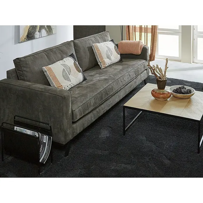 Teppichfliese Amazing - Hochflor, 100 % Polyester, Anthrazit - Gemütliches Wohnzimmer mit einem grauen Sofa, Kaffeetisch und dunklem Teppich. Die Kissen auf dem Sofa sind dekorativ gestaltet.