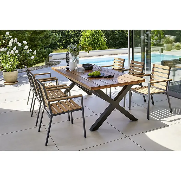 Sunfun Carina Gartenstuhl - Akazie, Stapelbar, Natur, B x T x H: 57,5 x 61 x 86 cm - Gartenset mit einem Holztisch und sechs Stühlen. Das Set steht auf einer Terrasse im Freien mit einem Pool im Hintergrund.