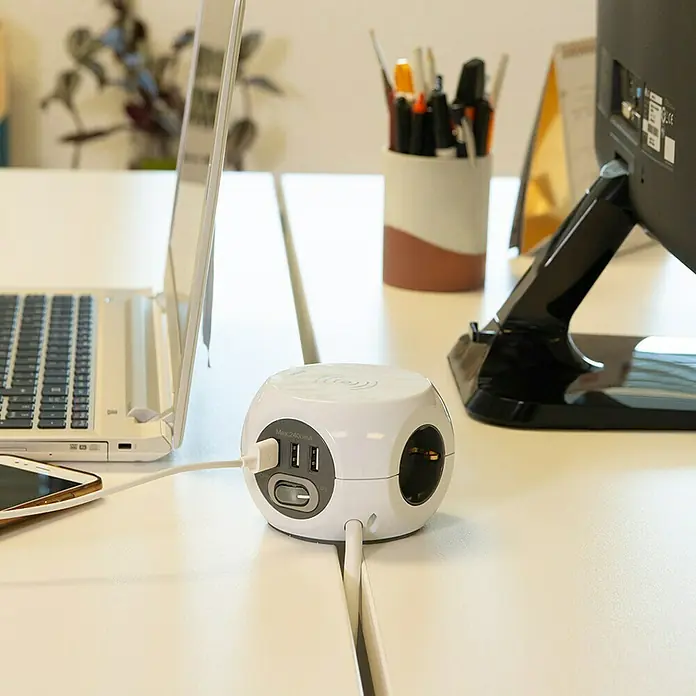 Simon Bola de enchufes con USB + carga inalámbrica Combi Ball - x 3, Blanco, 1,4 m, IP20 - Un adaptador de corriente cúbico blanco con puertos USB y toma de corriente en un escritorio, con dispositivos electrónicos.
