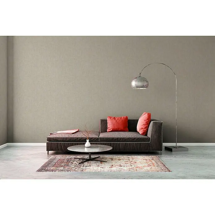 A.S. Création Greenery Vliestapete Borneo - Beige/Creme, Uni, 10,05 x 0,53 m - Ein modernes Wohnzimmer mit einem grauen Sofa, roten Kissen, einem Teppich und einer Stehlampe. Der Raum wirkt einladend und stilvoll.