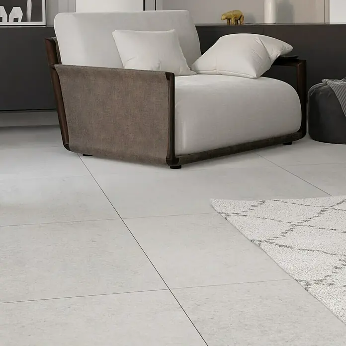 Feinsteinzeugfliese Erawan Grey - 100 x 100 cm, Grau, Matt - Elegante Nahaufnahme eines Sessels mit braunen Armlehnen und hellen Kissen auf einem hellen Boden.