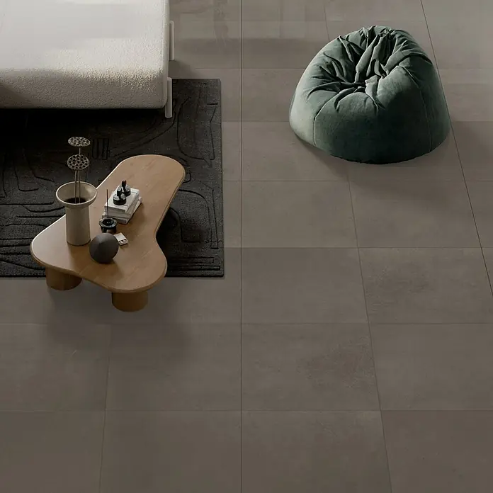 Art-Tec by Palazzo Feinsteinzeugfliese - 59,5 x 59,5 cm, Taupe, Glänzend - Das Bild zeigt eine moderne Inneneinrichtung mit einem stilvollen Couchtisch und einem bequemen Sitzsack auf einem grauen Fliesenboden.