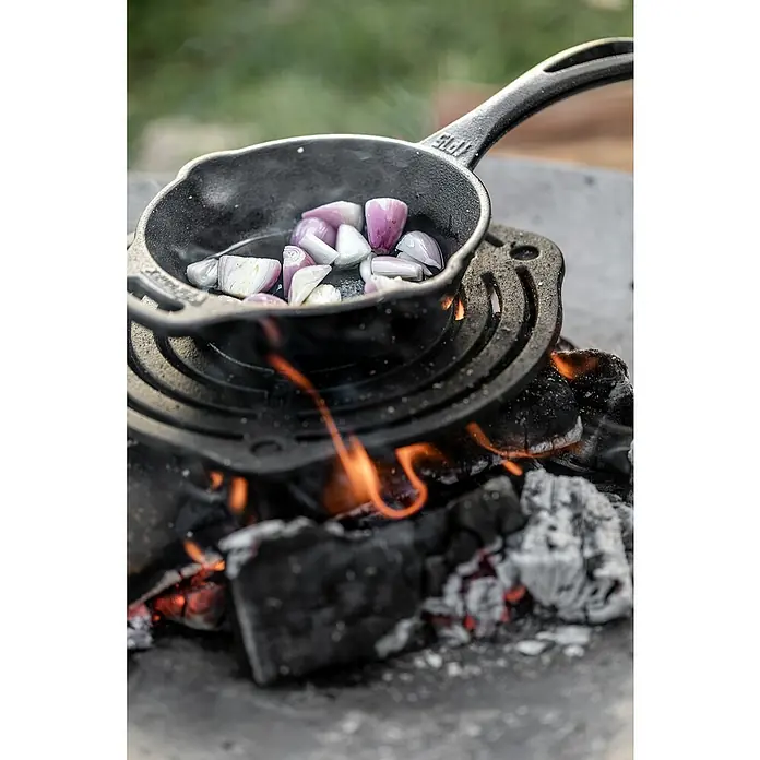 Petromax Gussrost Einsatz - Durchmesser: 23 cm, Gusseisen - Ein Mini-Gusseisenpfanne mit gehackten Schalotten auf einem Grill über einem offenen Feuer, bereit zum Kochen. Rustikales Kocherlebnis im Freien.