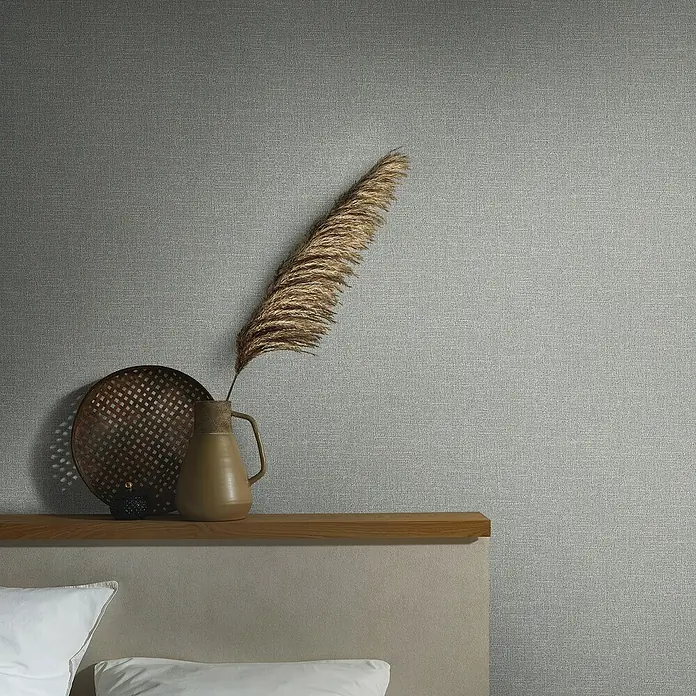 Marburg Eclectic Vliestapete - Mittelgrau, Uni, 10,05 x 0,7 m - Stillleben mit einer Vase und einem Tablett auf einem Regal vor einer grauen Wand mit Textur.