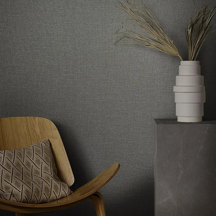 Marburg Eclectic Vliestapete - Anthrazit-Kupfer, Uni, 10,05 x 0,7 m - Nahaufnahme eines Raumes mit einem dekorativen Stuhl, einem Zierkissen und einer eleganten Vase auf einem Sockel, die das Interieur aufwertet.