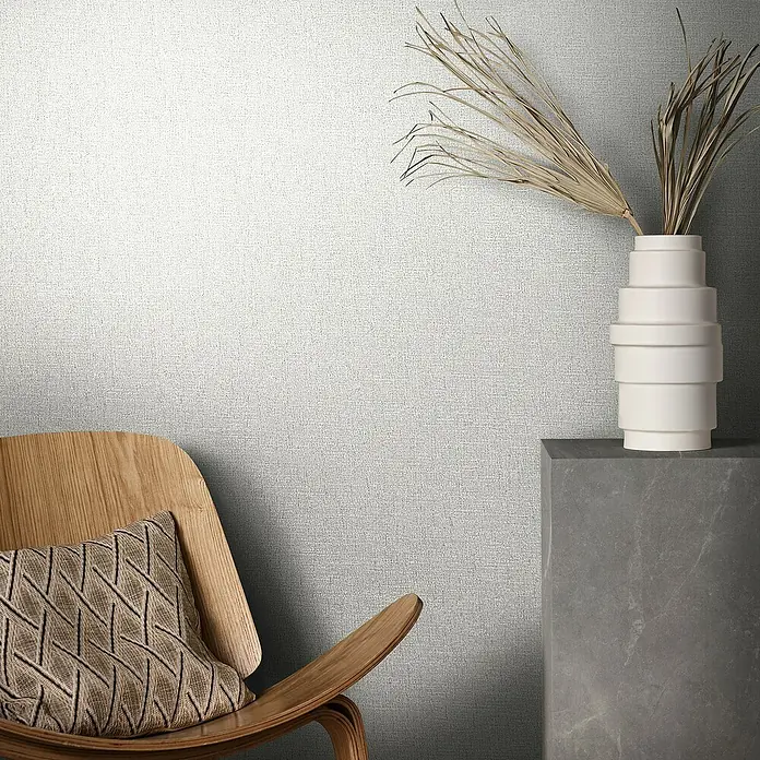 Marburg Eclectic Vliestapete - Helles Beige, Uni, 10,05 x 0,7 m - Ein Interieur mit einem eleganten Stuhl mit Kissen und einer Vase mit trockenem Pampasgras vor einer strukturierten Wand.