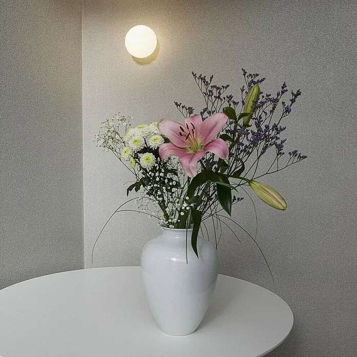 Marburg Eclectic Vliestapete - Lichtgrau, Uni, 10,05 x 0,7 m - Stillleben mit weißer Vase, gefüllt mit rosa Lilien, Schleierkraut und lila Zierblumen auf einem weißen Tisch, beleuchtet von einer Wandleuchte.