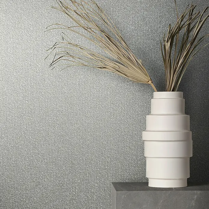 Marburg Eclectic Vliestapete - Grau, Uni, 10,05 x 0,7 m - Nahaufnahme einer modernen weißen Vase mit dekorativen getrockneten Pflanzen auf einer grauen Oberfläche vor einer strukturierten Wand.