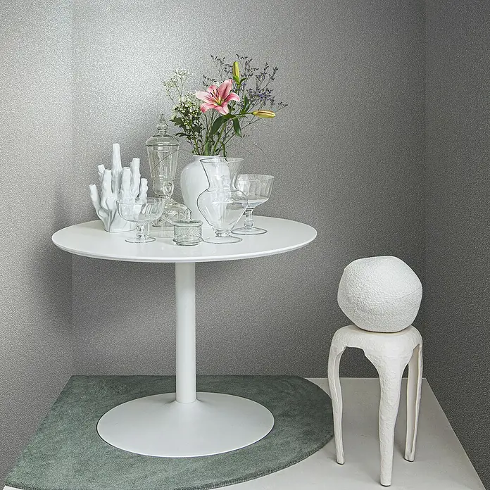 Marburg Eclectic Vliestapete - Grau, Uni, 10,05 x 0,7 m - Eine Nahaufnahme eines stilvollen Interieurs mit einem runden Tisch, diversen Glaswaren, Blumenarrangement und einer skulpturalen weißen Dekoration.