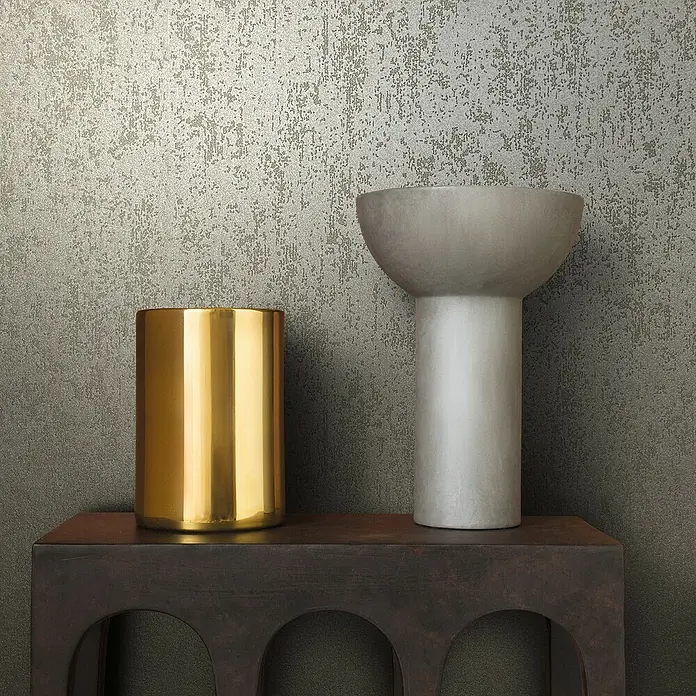 Marburg Eclectic Vliestapete Glasperlenstruktur - Dunkelbeige, Metalloptik, 10,05 x 0,7 m - Goldener Zylinder und graue Vase auf einem dunklen Regal vor einer strukturierten Wand. Elegante Dekoartikel für ein stilvolles Zuhause.