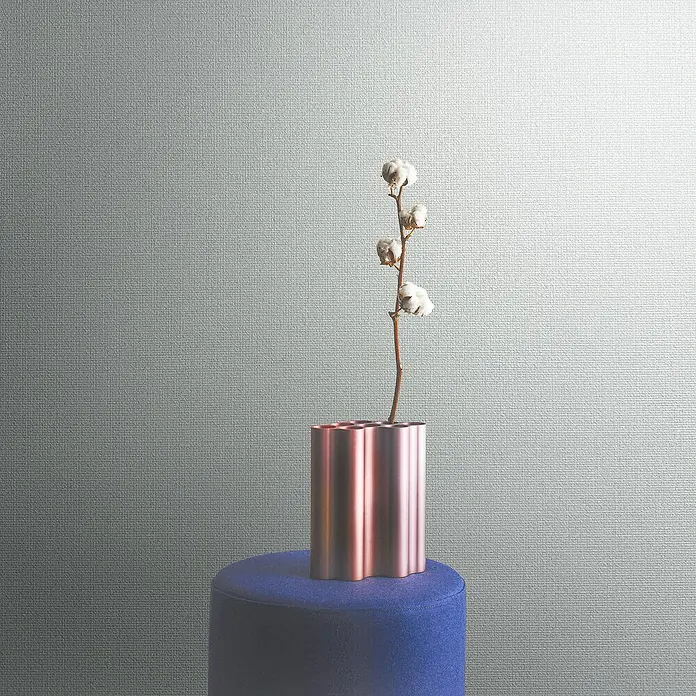 Marburg Eclectic Vliestapete - Weiß, Uni, 10,05 x 0,7 m - Dekorative Nahaufnahme einer modernen, roségoldenen Vase mit Baumwollzweig, platziert auf einem blauen Hocker vor einem grauen Hintergrund.