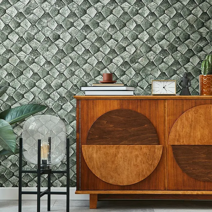 Marburg Eclectic Vliestapete Pentagonmuster - Grüngrau, Grafisch, 10,05 x 0,7 m - Nahaufnahme eines Sideboards aus Holz mit runden Verzierungen und Dekorationen wie einer Lampe, einer Statue und einer Pflanze.