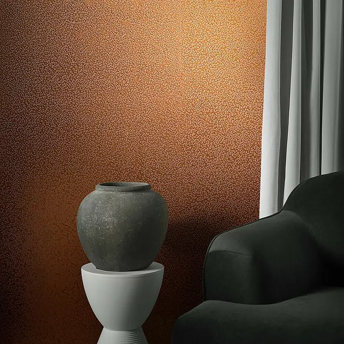 Marburg Eclectic Vliestapete Hammerschlag-Optik - Kupfer, Metalloptik, 10,05 x 0,7 m - Nahaufnahme einer stilvollen grauen Vase auf einem weißen Sockel, vor einer strukturierten Wand und einem eleganten Sessel.