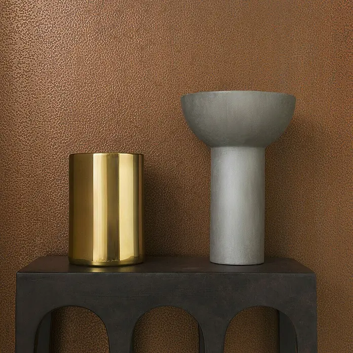 Marburg Eclectic Vliestapete Hammerschlag-Optik - Kupfer, Metalloptik, 10,05 x 0,7 m - Ein goldenes Gefäß und eine graue Vase stehen auf einem dunklen Tisch vor einer braunen Wand.