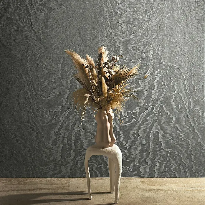 Marburg Eclectic Vliestapete Moiré - Anthrazit, Metalloptik, 10,05 x 0,7 m - Ein einzigartiges Arrangement mit einem beigen Gefäß auf einem Hocker, das eine Auswahl an Trockenblumen und Gräsern kunstvoll präsentiert.