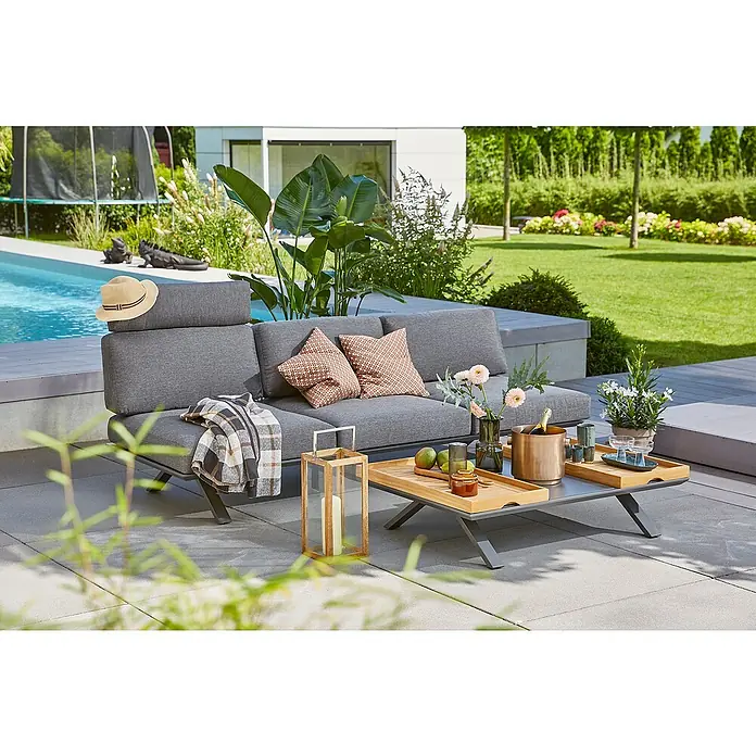 Sunfun Loungemöbel-Set Lumar - 5 -tlg., Aluminium, Teak, mit Kopfstütze, Night-Grey - Ein graues Outdoor-Sofa mit Kissen und einer Decke, sowie ein Tisch mit Getränken und Dekorationen auf einer Terrasse.
