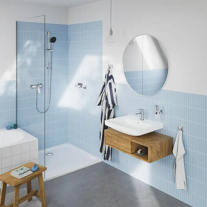 Grohe QuickFix Brausegarnitur - Lochabstand: 47 cm - 62 cm, Anzahl Strahlarten: 2 Stk. - Modernes Badezimmer-Interieur mit stilvollem Waschtischunterschrank aus Holz, ovalem Spiegel und blauen Akzentfliesen für ein frisches Ambiente.